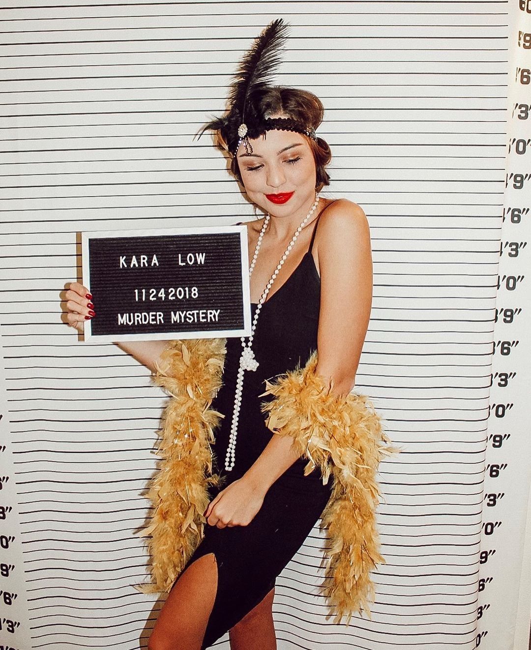 Woman in a black dress holding a 'Murder Mystery' sign.