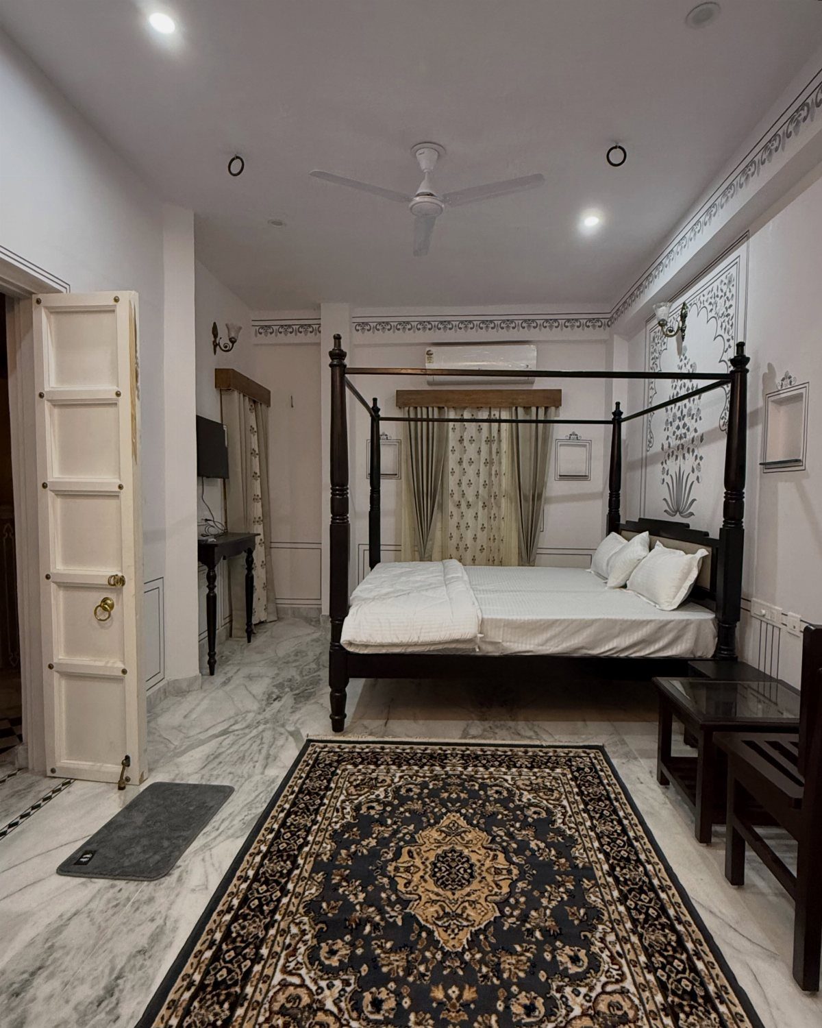 A four-poster bed with white linens sits on a marble floor in a hotel room.