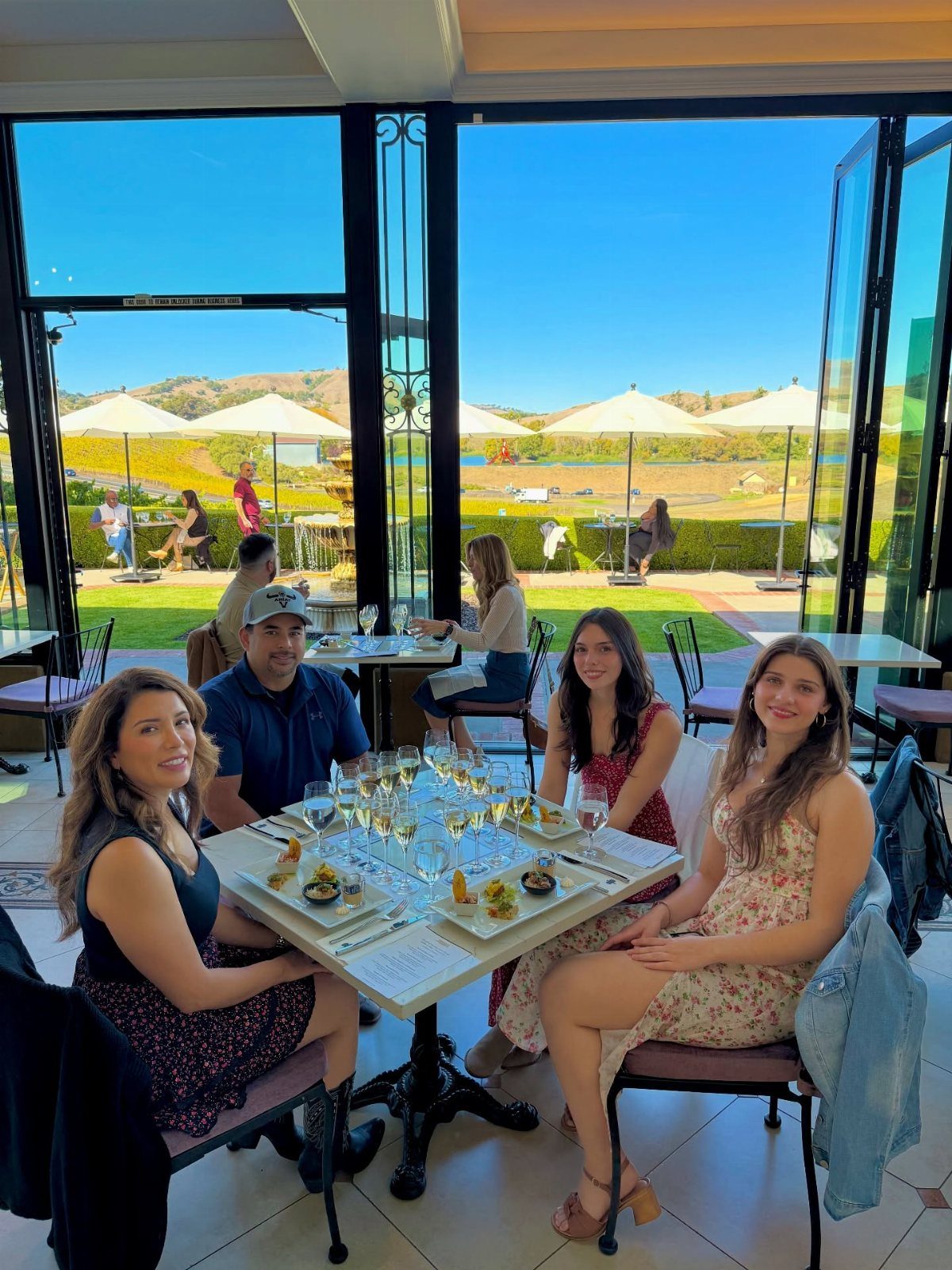 Four friends enjoying champagne and food at a sunny restaurant.