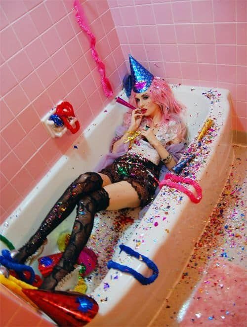 Person in a bathtub surrounded by colorful confetti and party decorations.