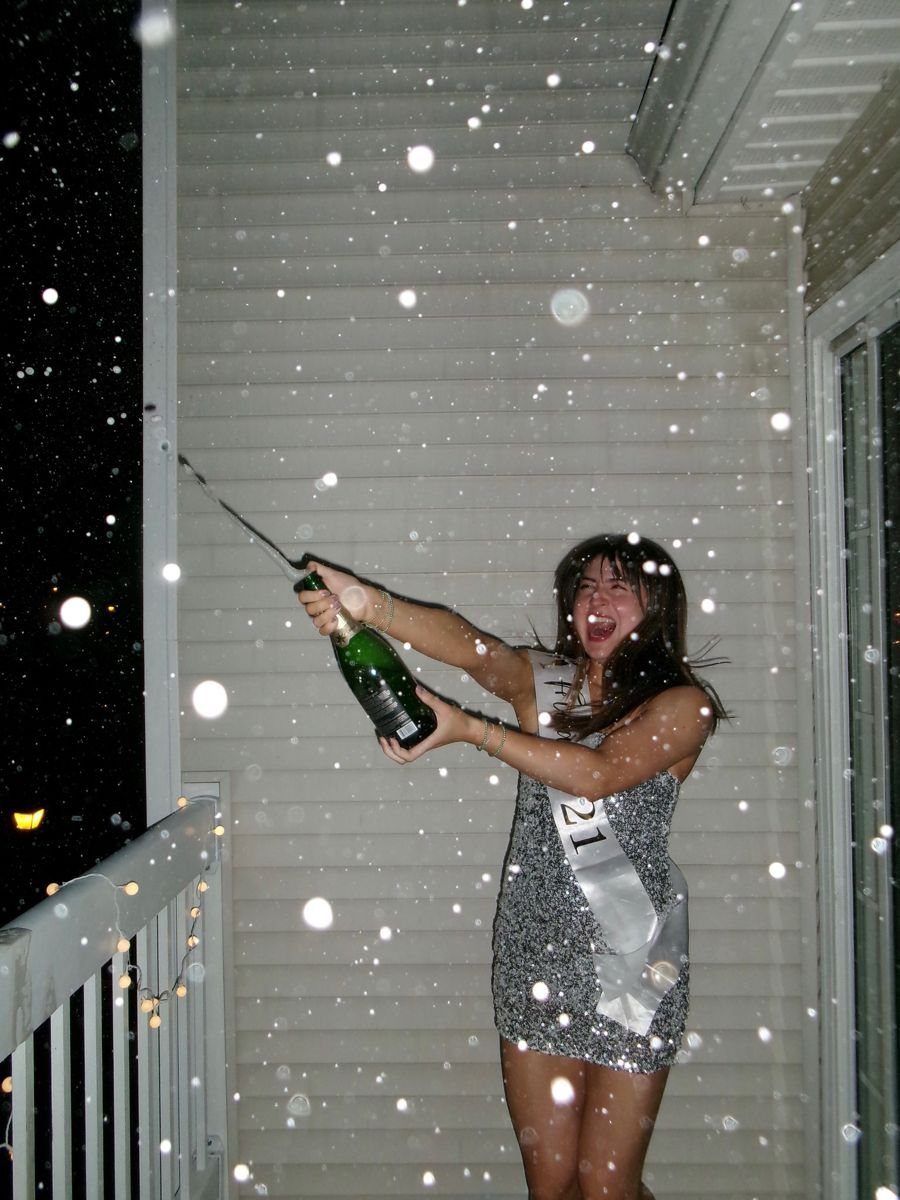 Young woman joyfully popping champagne on a snowy balcony.