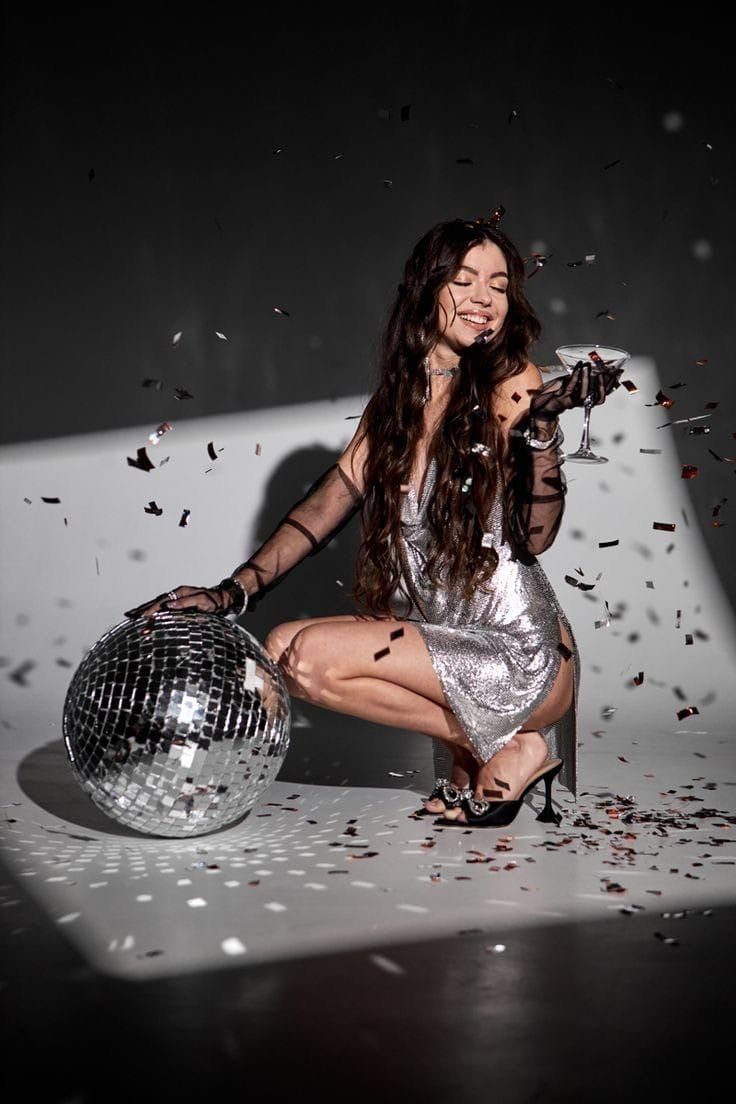Woman in silver dress poses with disco ball and confetti.