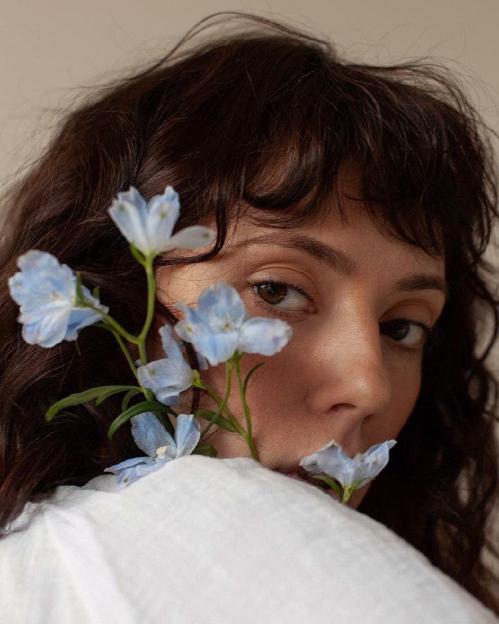 A person with dark wavy hair looking through small light blue flowers.