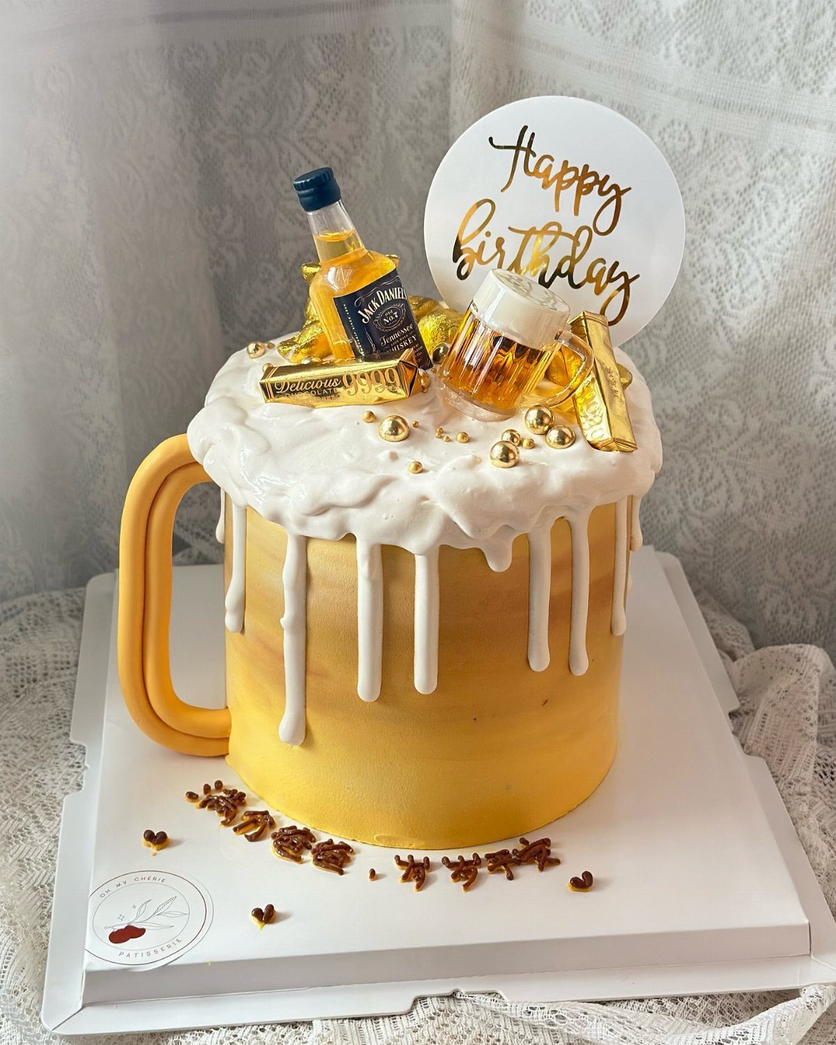 Yellow mug-shaped cake with white frosting foam, miniature liquor bottles, and a Happy Birthday sign.
