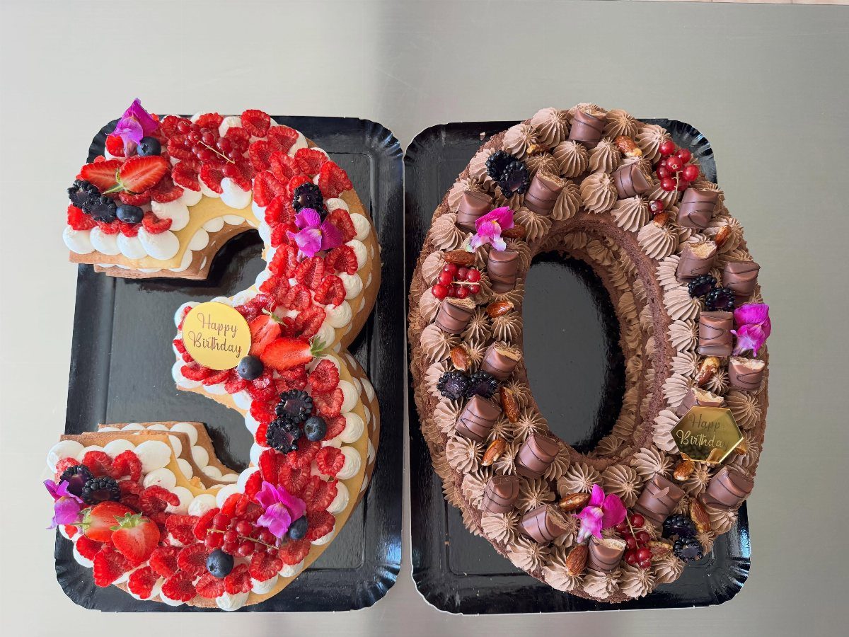 Number 30 shaped cakes decorated with fresh berries and frosting on black trays.
