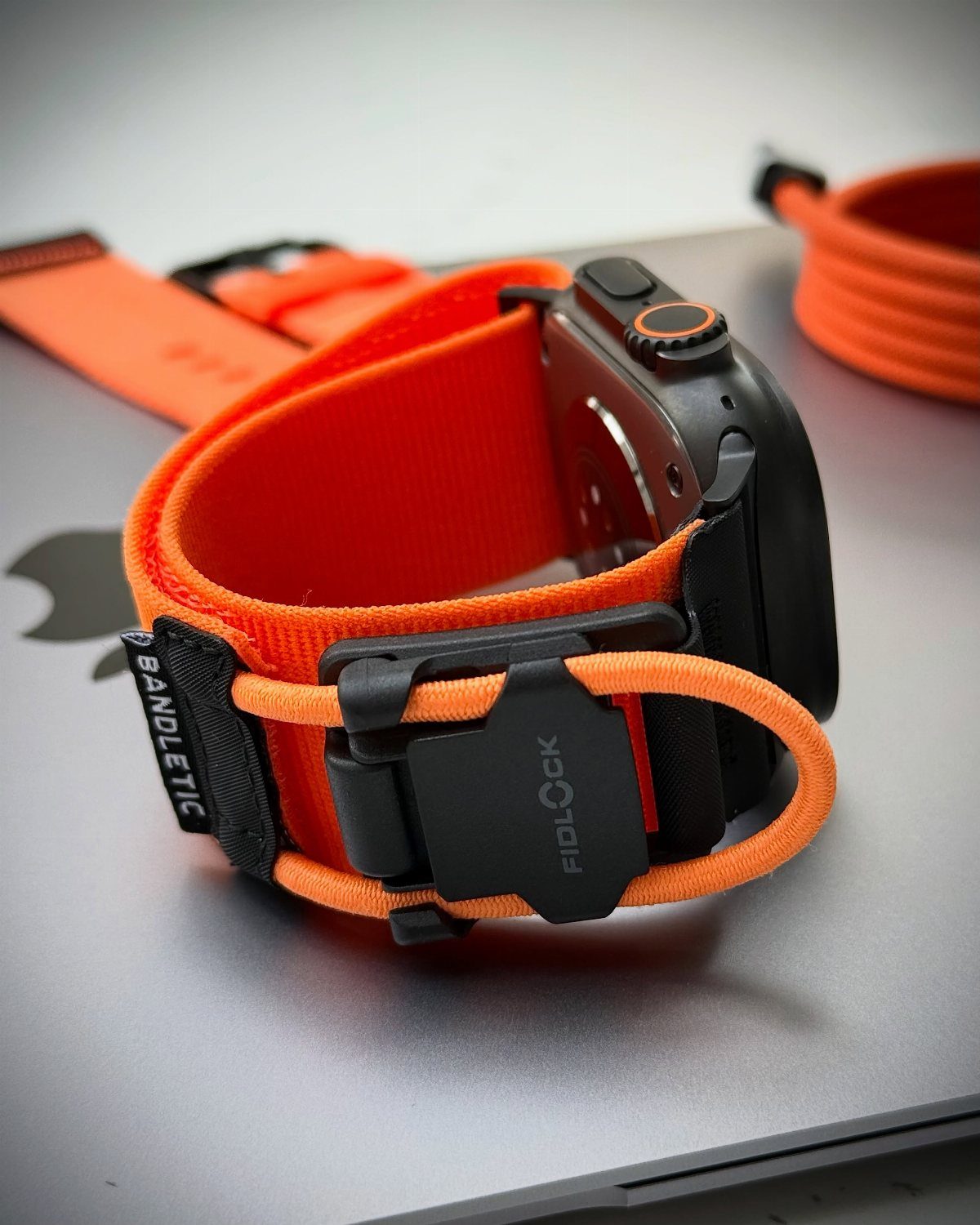 Bright orange breathable Apple Watch band with black magnetic clasp on a silver surface.