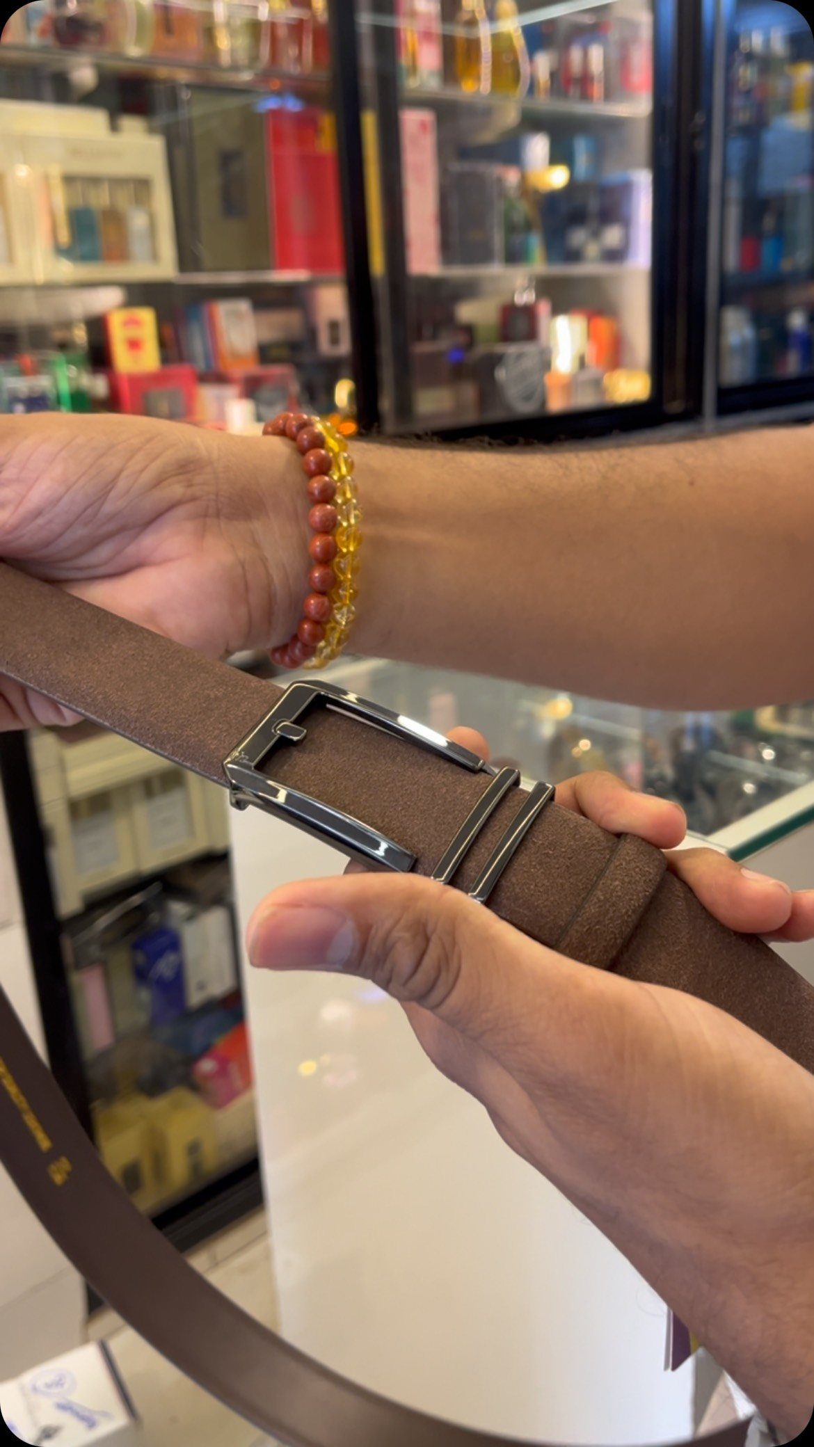 Hands holding a brown leather belt with a silver buckle in a retail store.