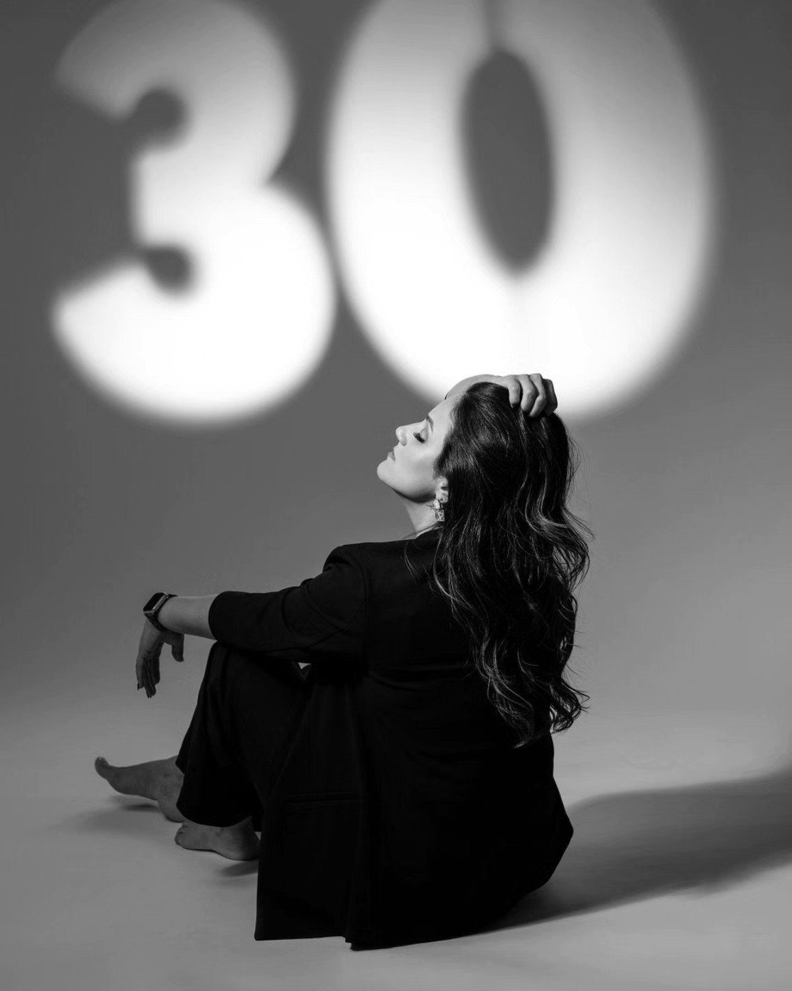 Woman in a black suit sitting on the floor with a large number thirty projected behind her.
