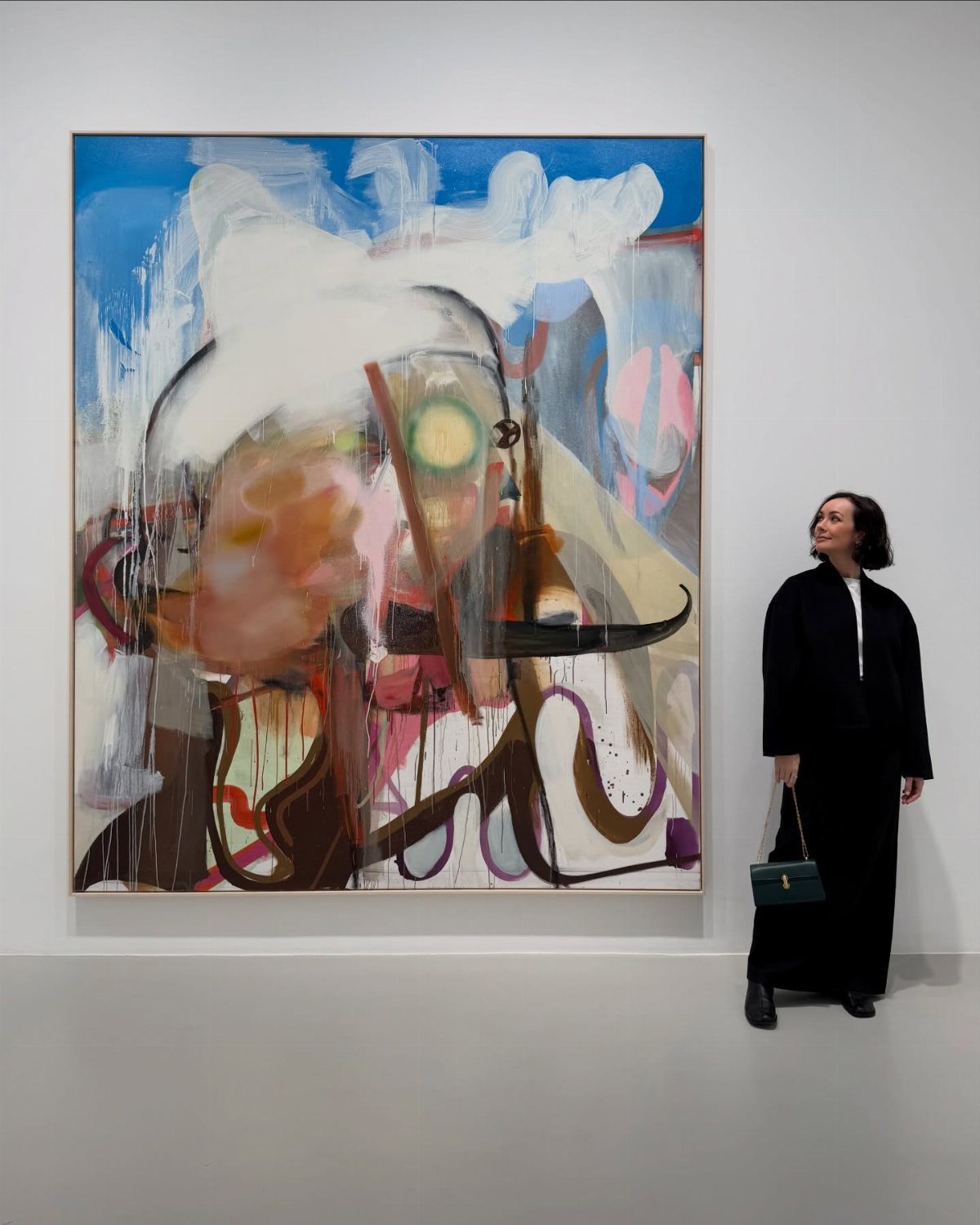 A woman in black clothing admires a large abstract painting in a bright art gallery.