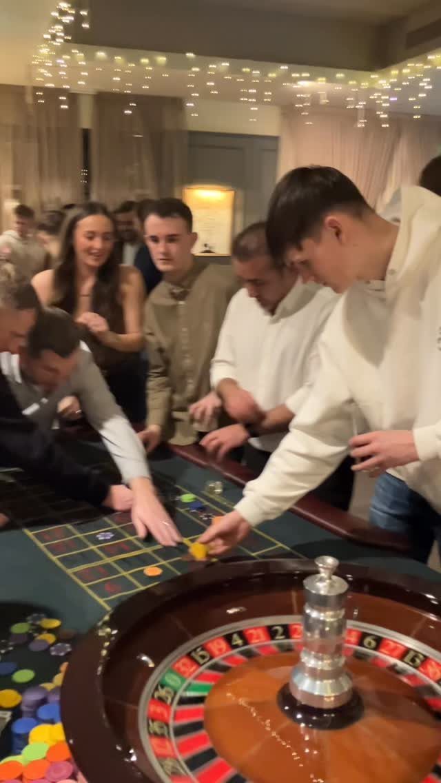 Young adults playing roulette and placing colorful chips on a casino table.