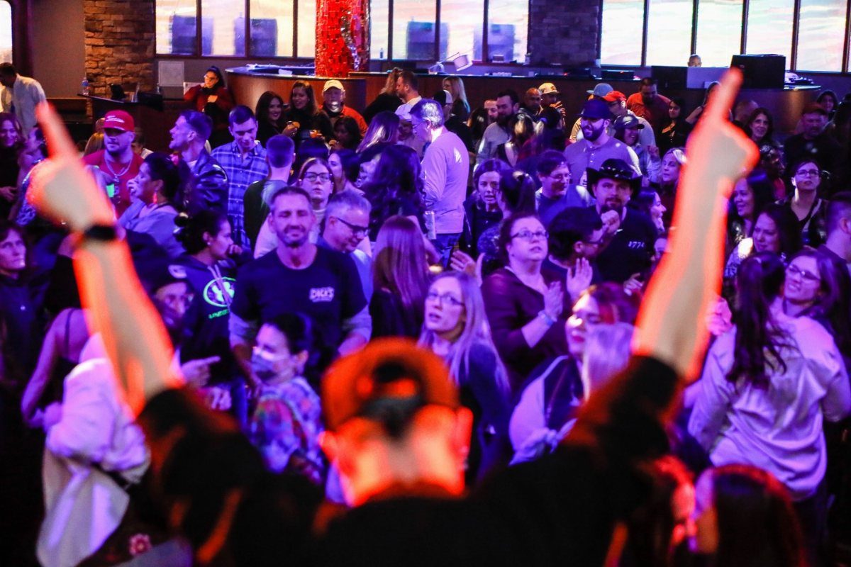 A crowd of people gathered in a dimly lit club with colorful lights and raised hands.
