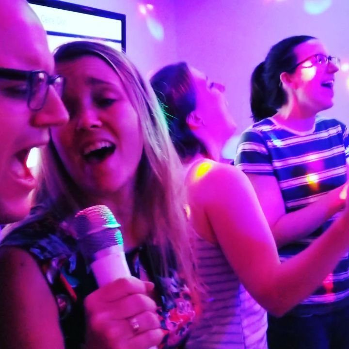 Group of friends singing joyfully with a microphone under colorful purple disco lights.