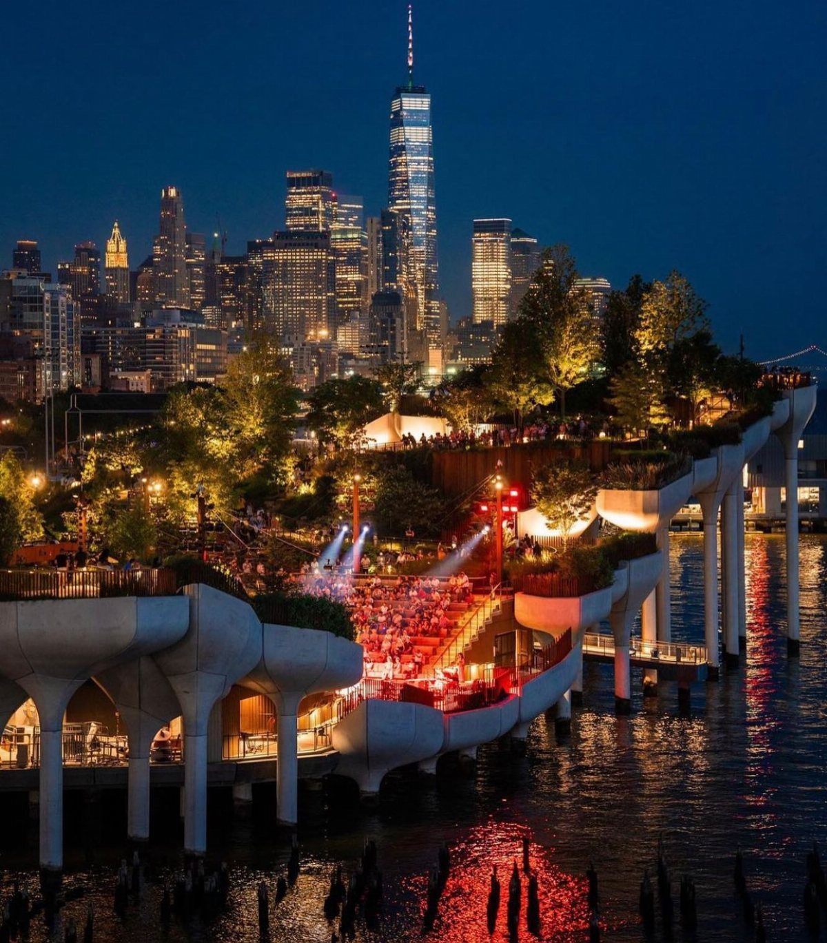 An outdoor concert venue with red lights set against a glowing city skyline at night.