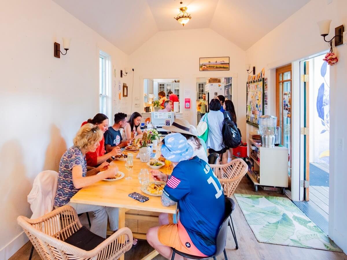 A group of friends sitting around a wooden table sharing a meal in a bright room.