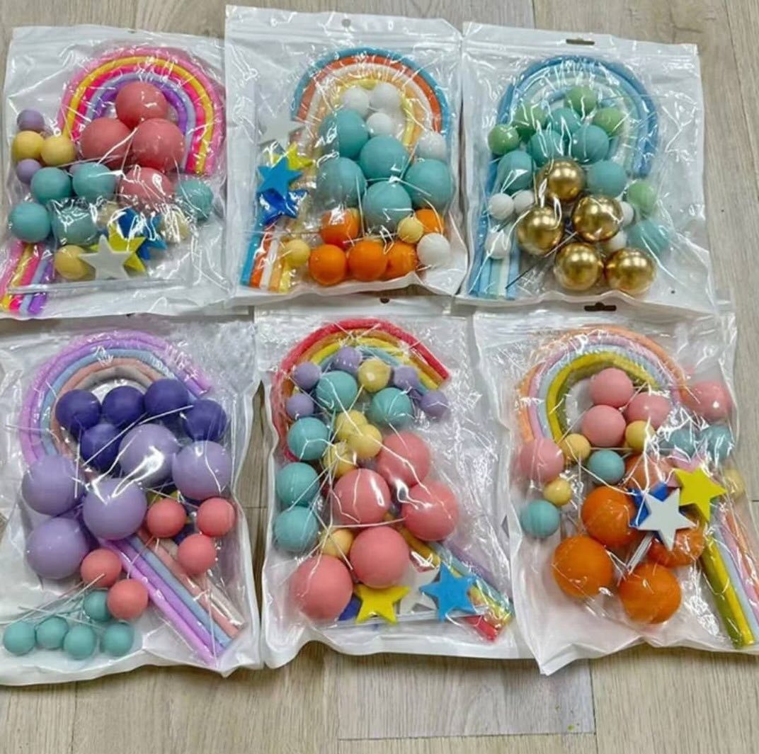 Six packages of colorful rainbow and star shaped cake topper decorations on a wooden surface.
