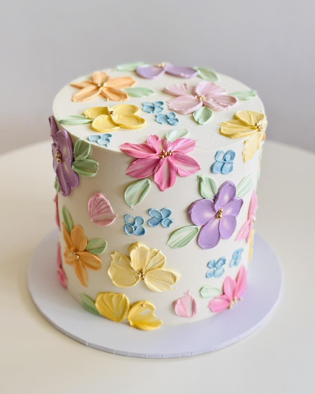 White buttercream cake decorated with colorful textured 3D floral designs in pastel colors.