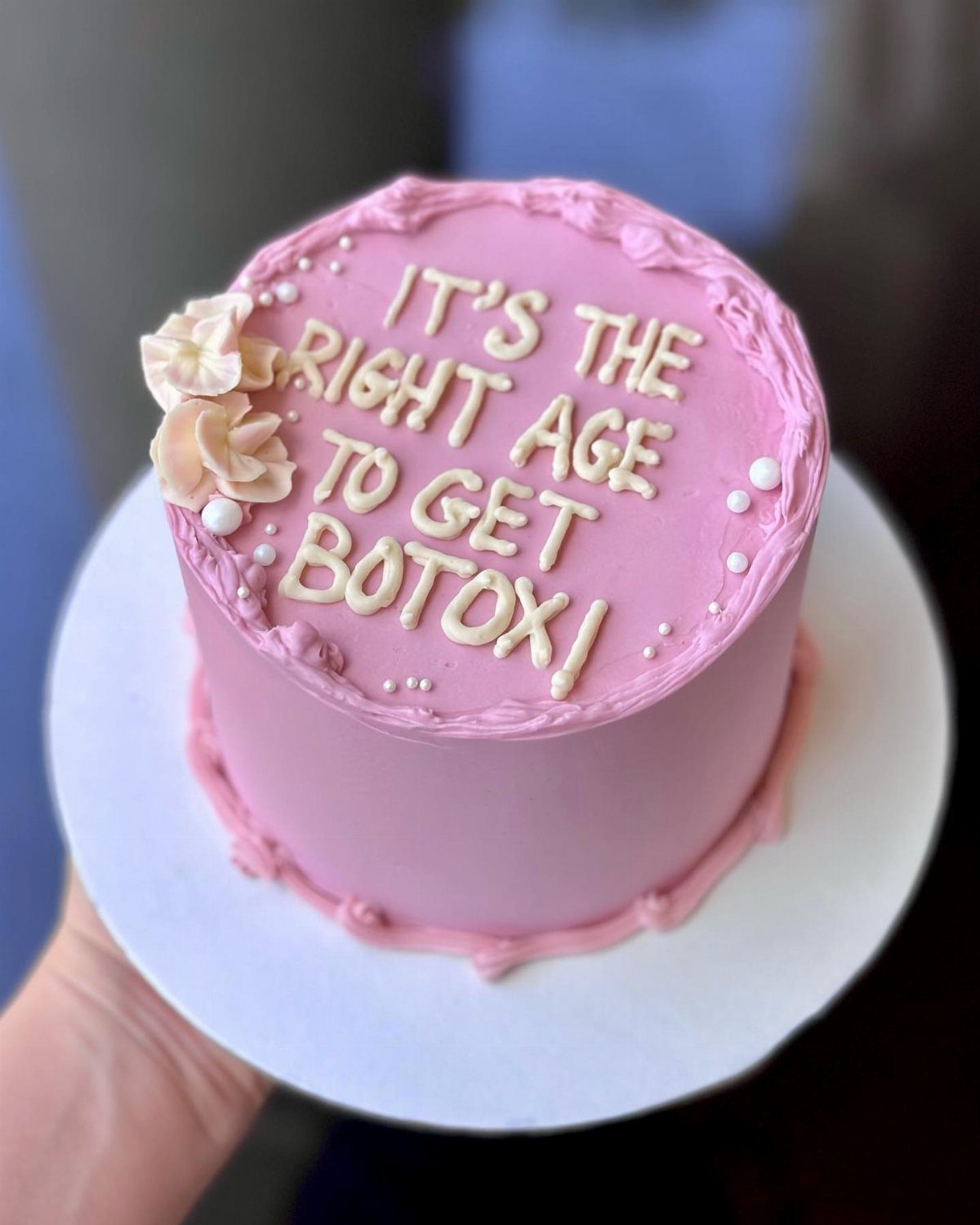 Pink frosted cake with humorous text about getting Botox held in a hand.