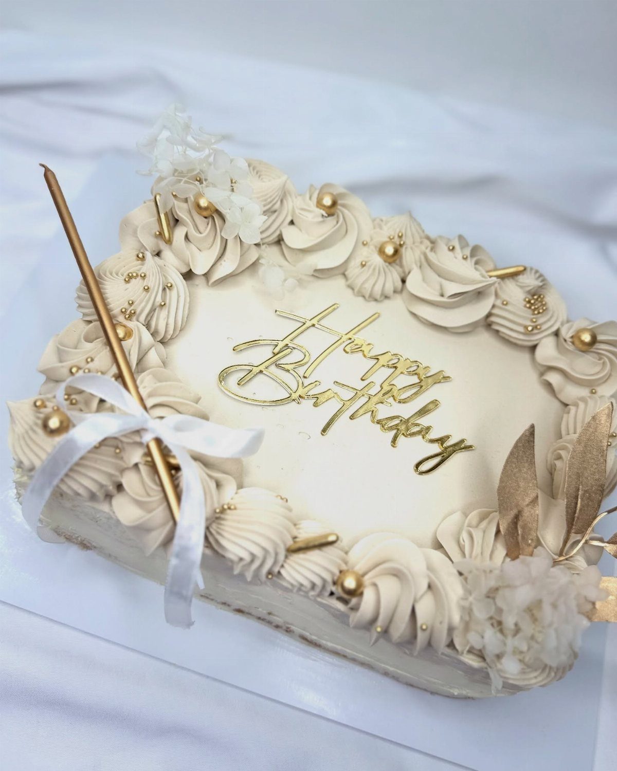 Square white birthday cake with gold lettering, cream swirls, and gold pearl decorations.