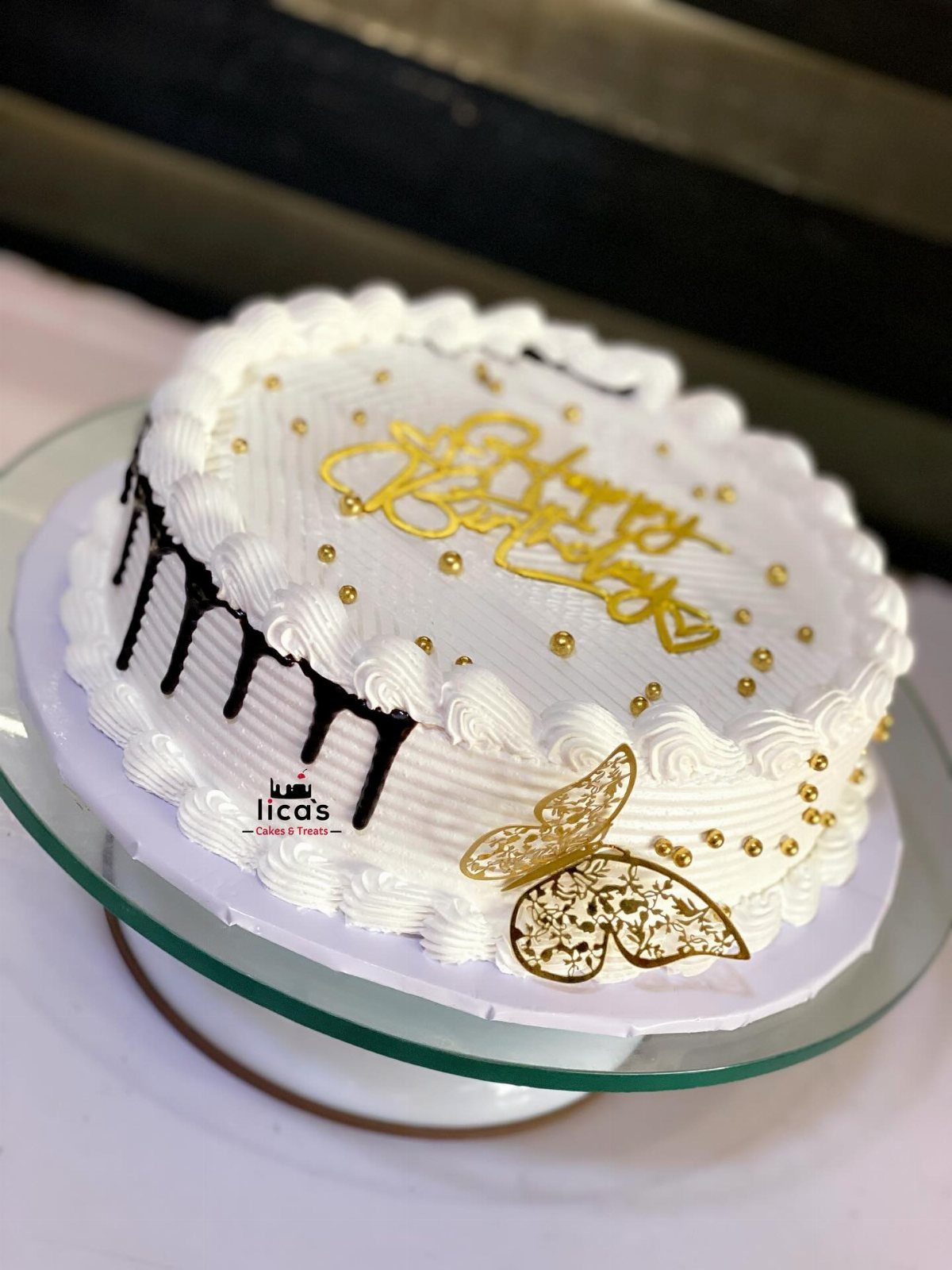 White frosted single tier cake with gold butterfly, gold pearls, and chocolate drips.