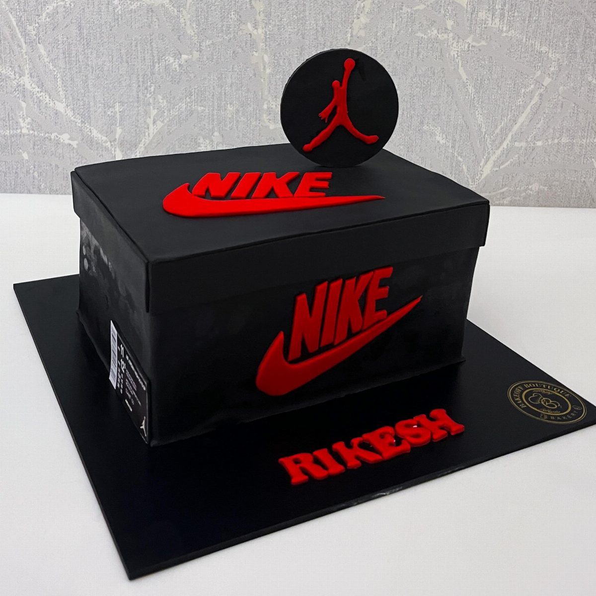 A black Nike shoebox shaped cake with red logos and a Jumpman topper.