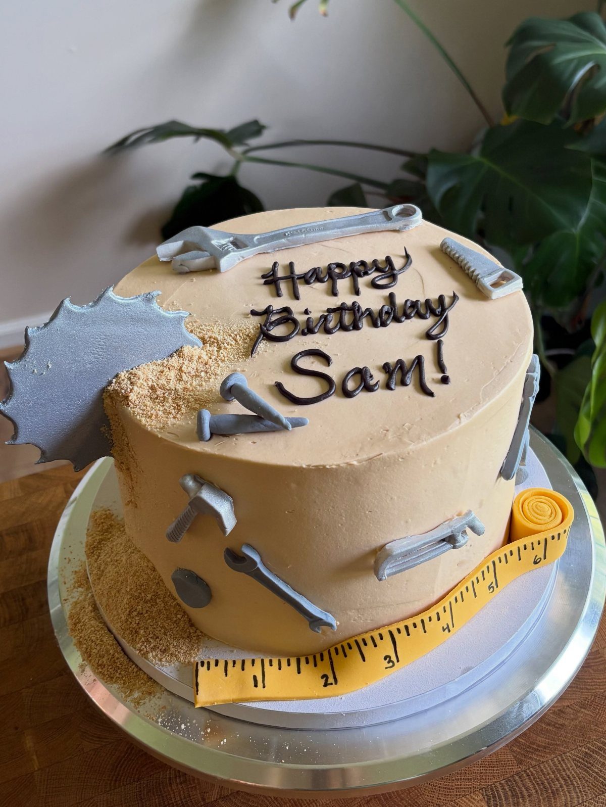 Handyman themed birthday cake with edible tools, sawdust crumbs, and a yellow measuring tape.