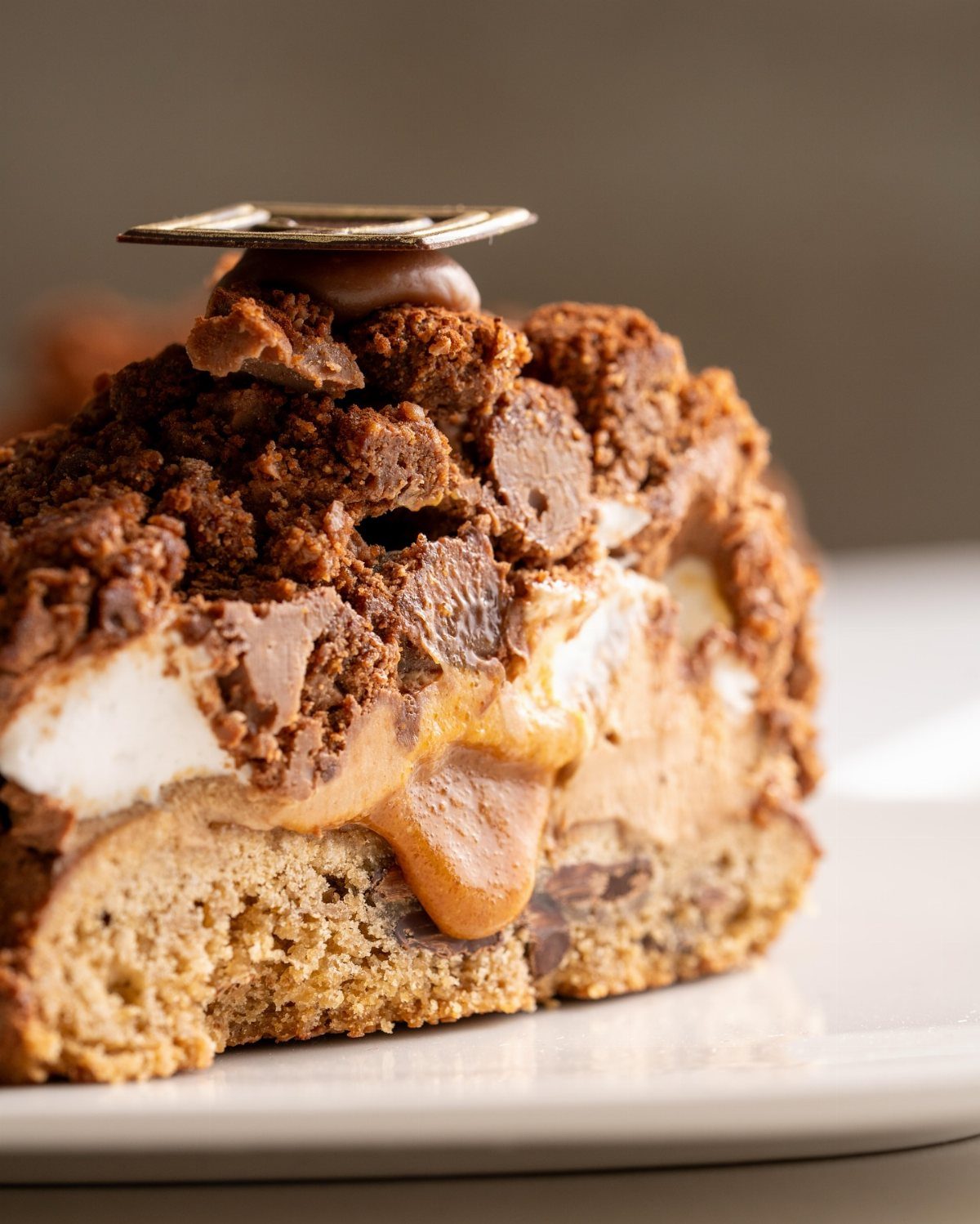 A slice of chocolate cake with marshmallow and fudge layers on a white plate.