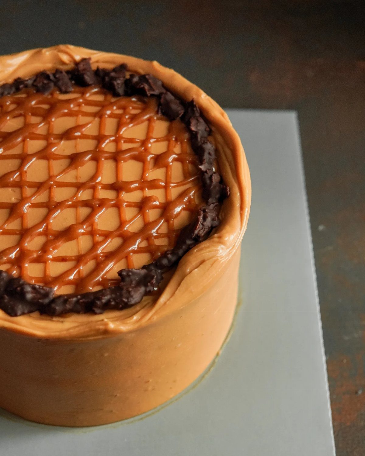 Caramel drip cake with a lattice sauce pattern and dark chocolate pieces on top.