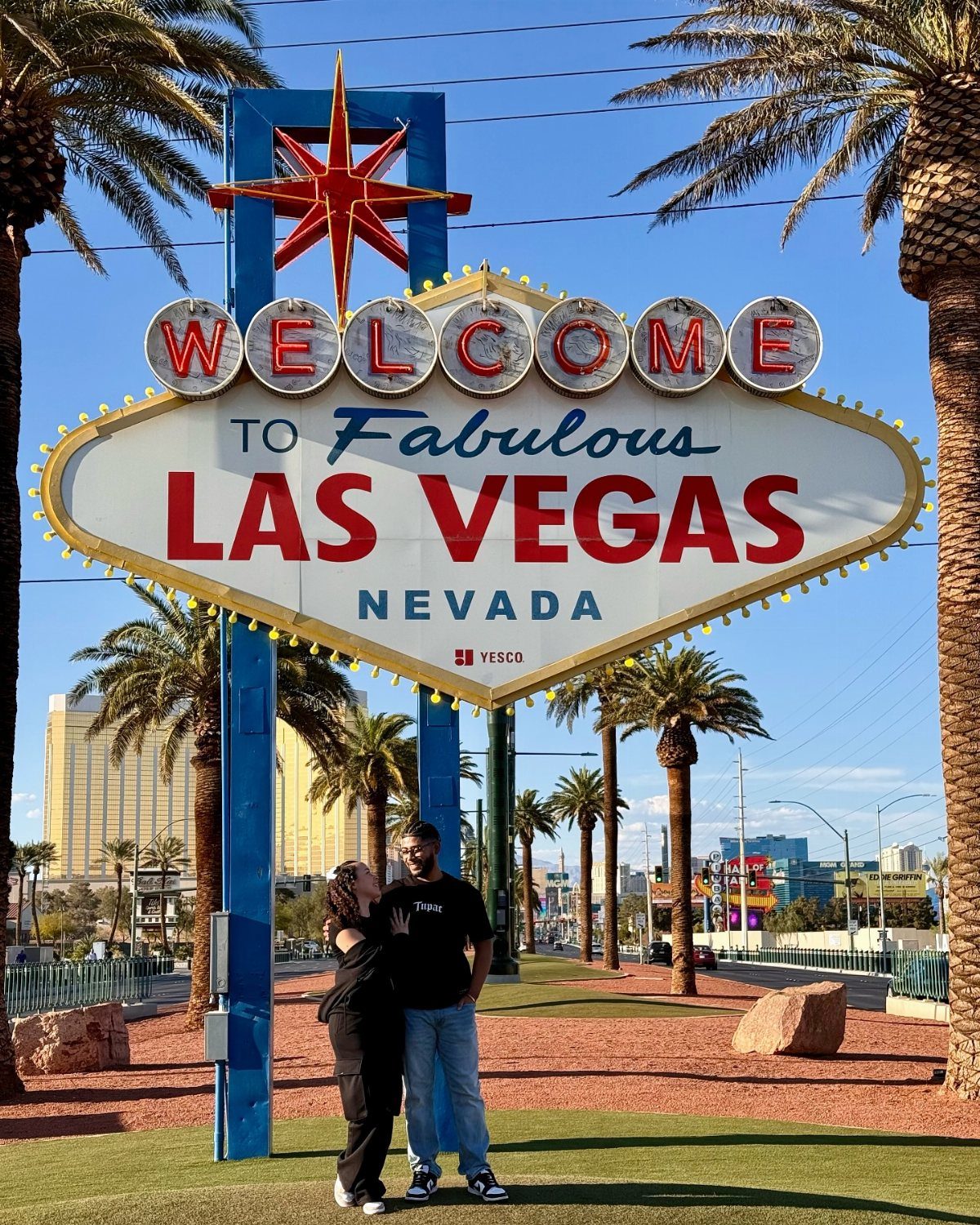 Two people posing in front of the iconic Welcome to Fabulous Las Vegas sign with palm trees.