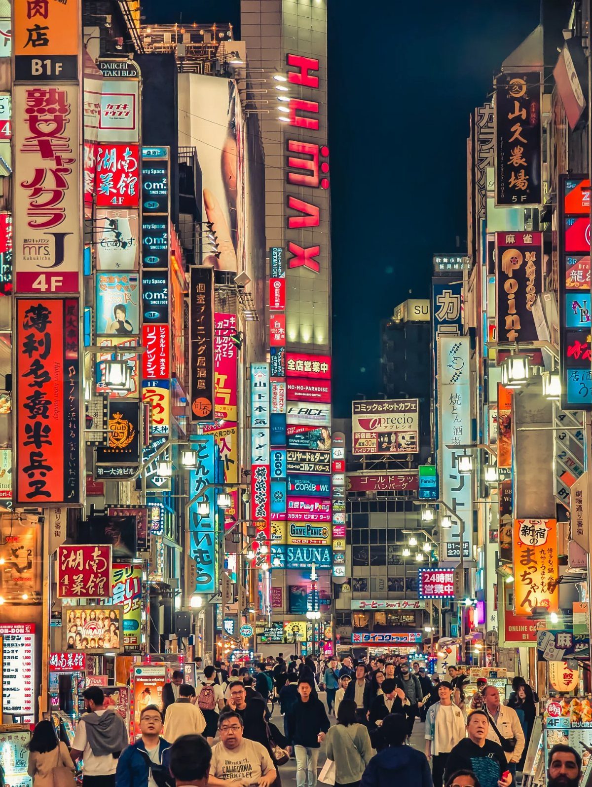 Crowded Tokyo street at night filled with glowing neon signs and many pedestrians walking below.