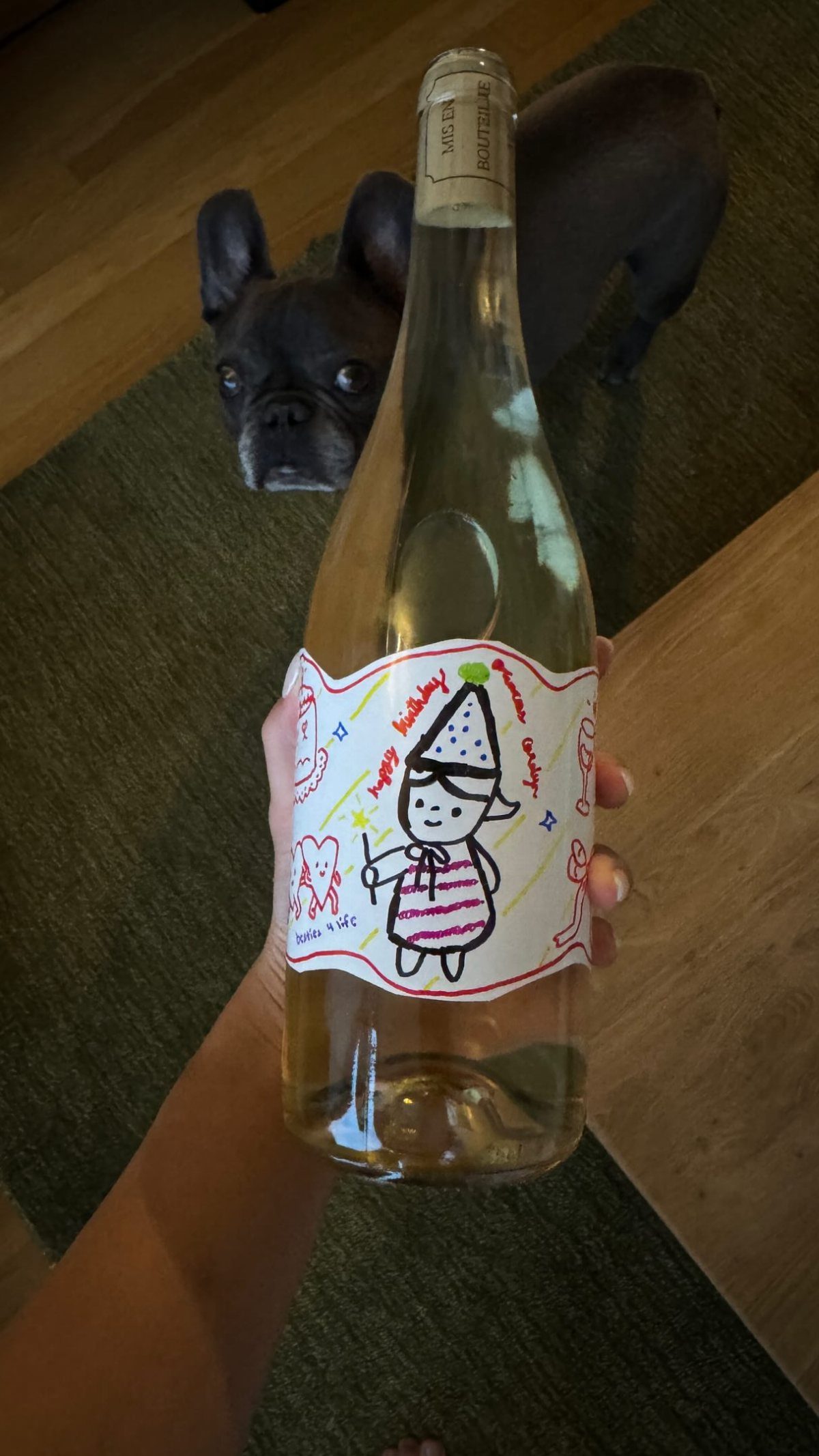 Hand holding a wine bottle with a custom hand-drawn birthday character label.