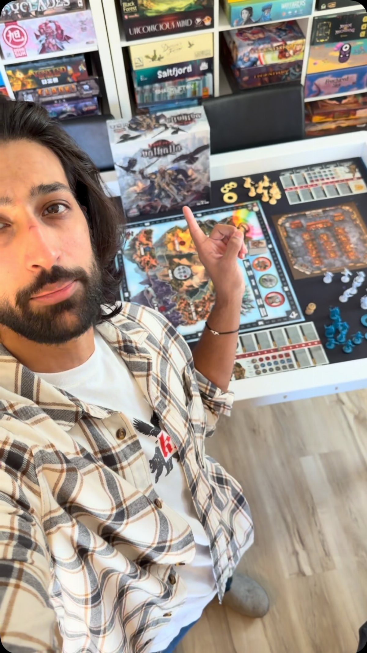 Man in a plaid shirt taking a selfie next to a detailed board game setup.