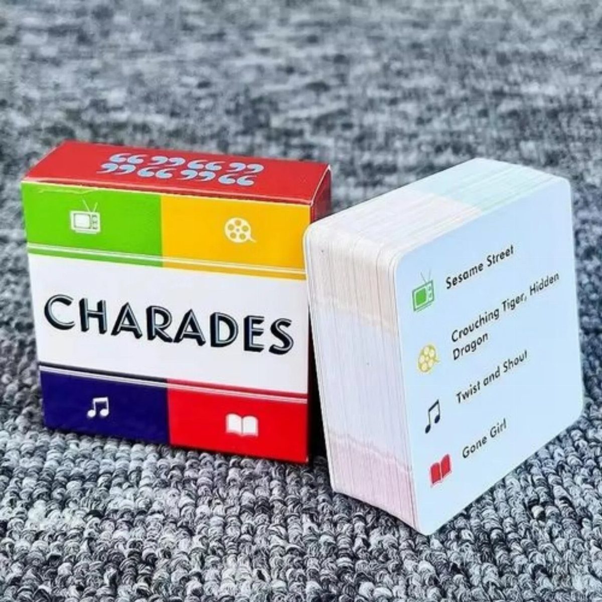 A colorful Charades game box next to a stack of white game cards on a grey surface.