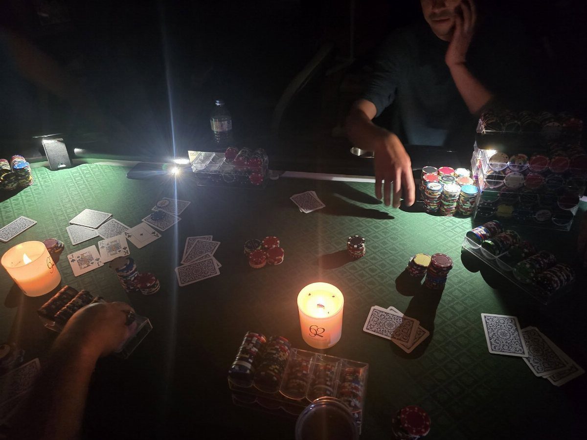Playing cards and stacks of poker chips scattered on a green felt table with lit candles.