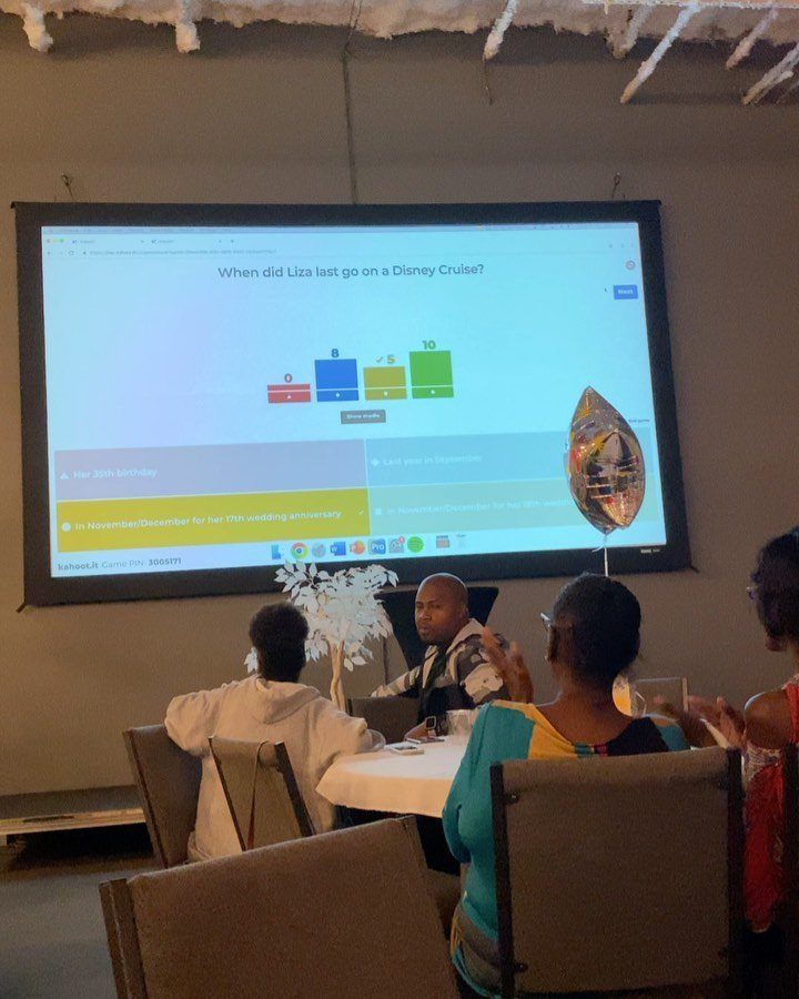 People sitting at a table watching a trivia question projected on a large screen.