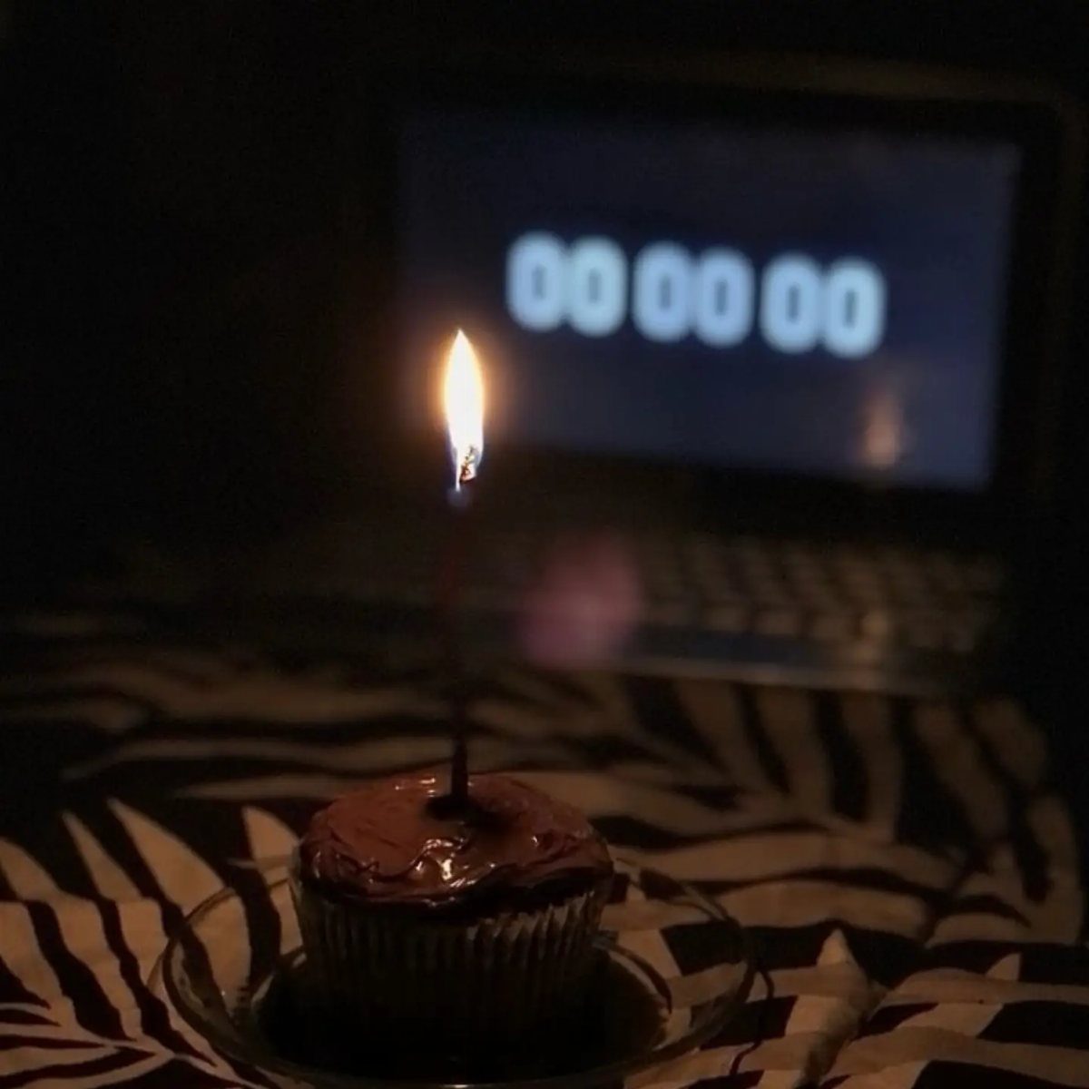 Chocolate cupcake with a lit candle in front of a laptop timer showing midnight.