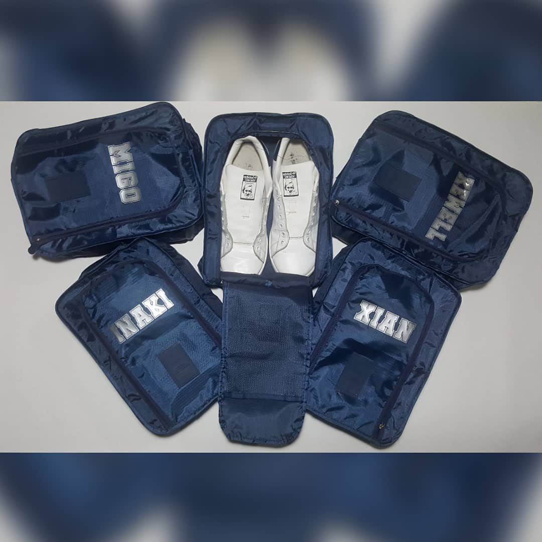 Five navy blue travel pouches with silver names, including two containing white sneakers.