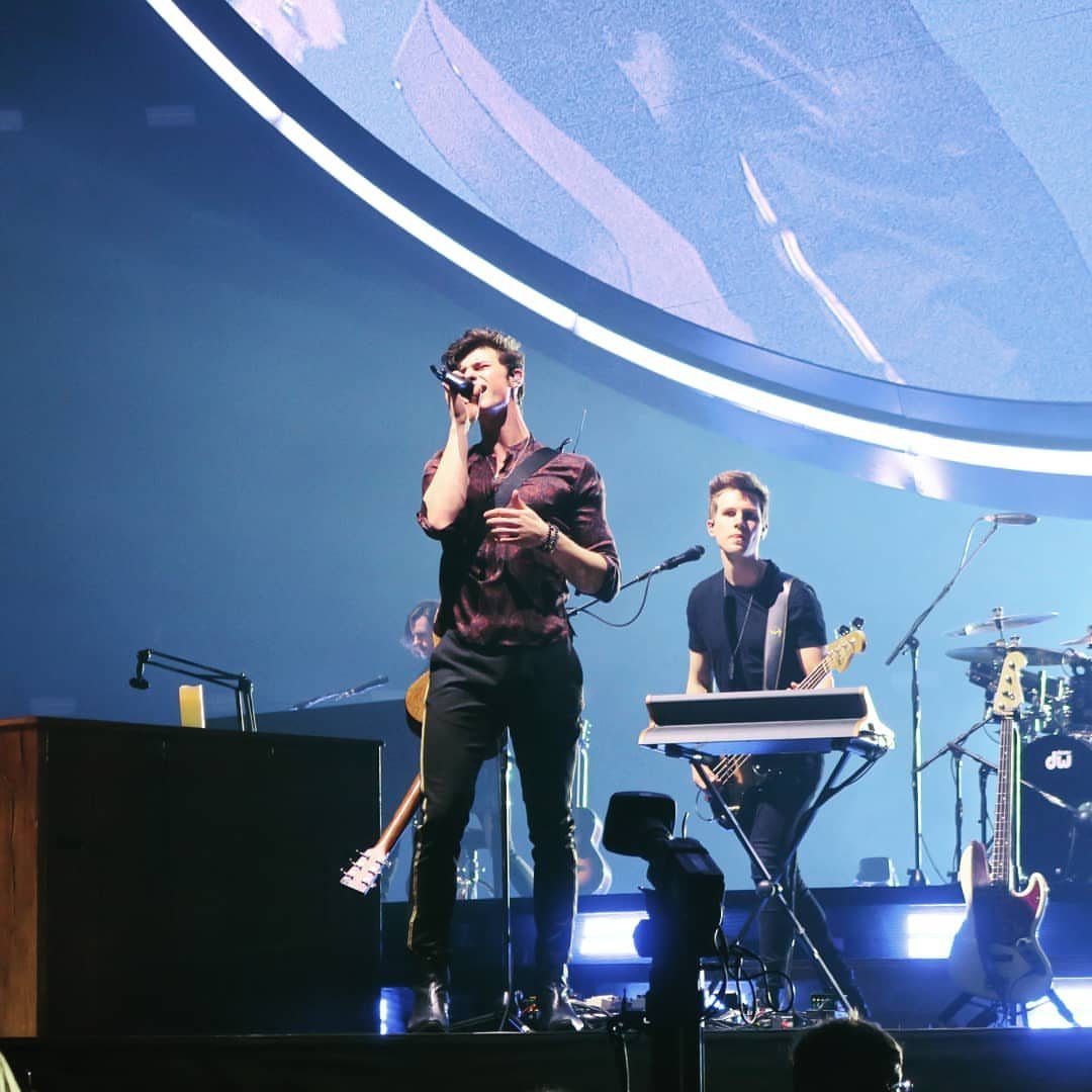 A male singer performing on a brightly lit stage with musicians and instruments.