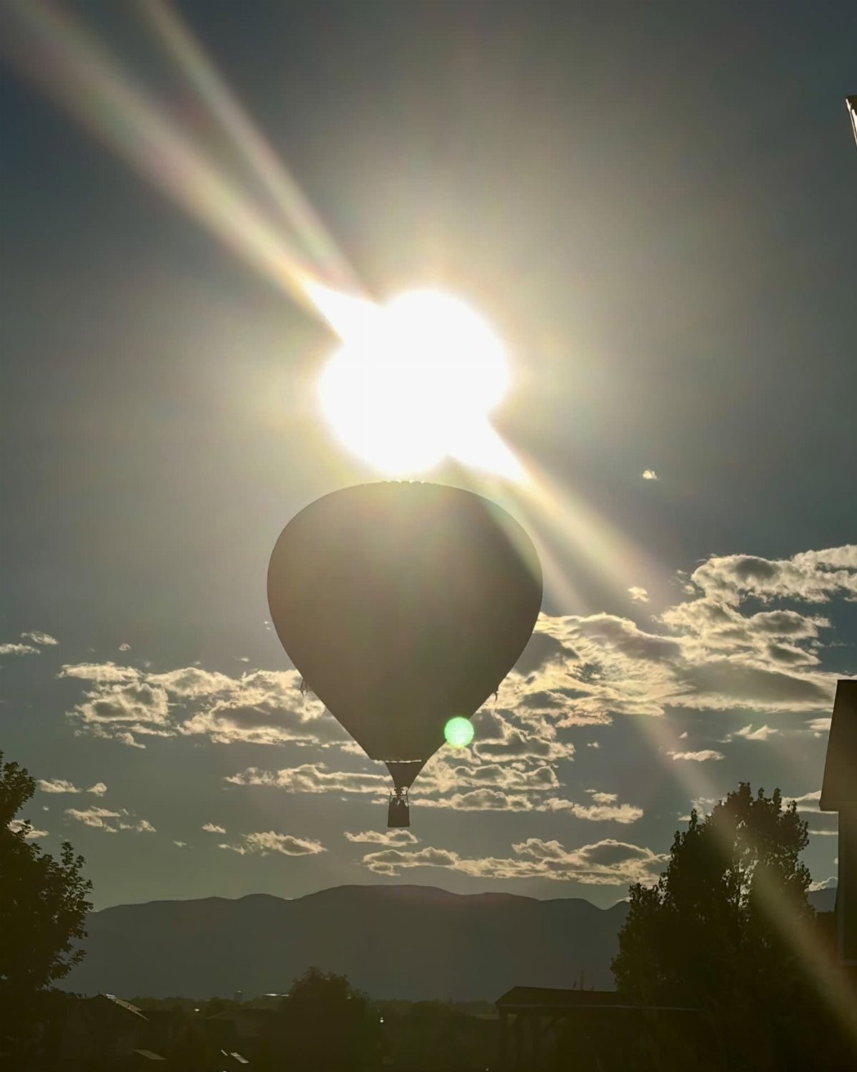A silhouette of a hot air balloon floating against a bright, sunlit sky with mountains below.