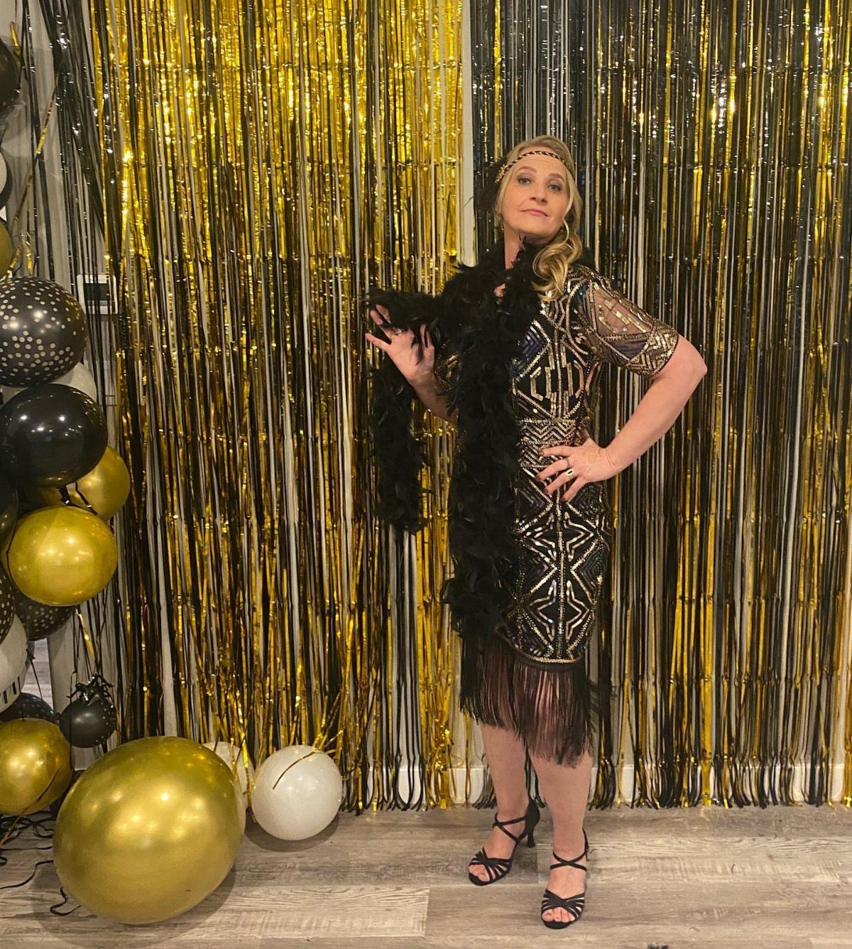 Woman in a gold flapper dress posing against a gold tinsel backdrop with balloons.