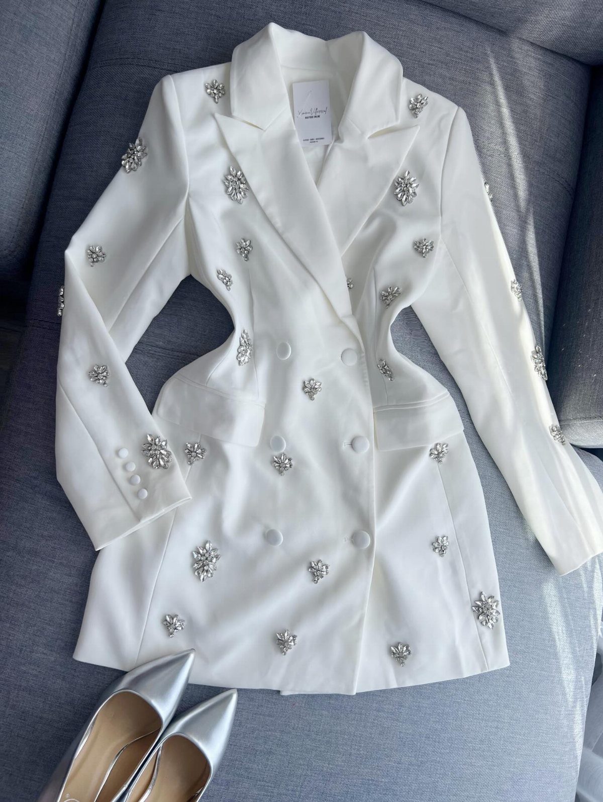 White blazer dress with silver rhinestone details laid on a grey surface with silver heels.