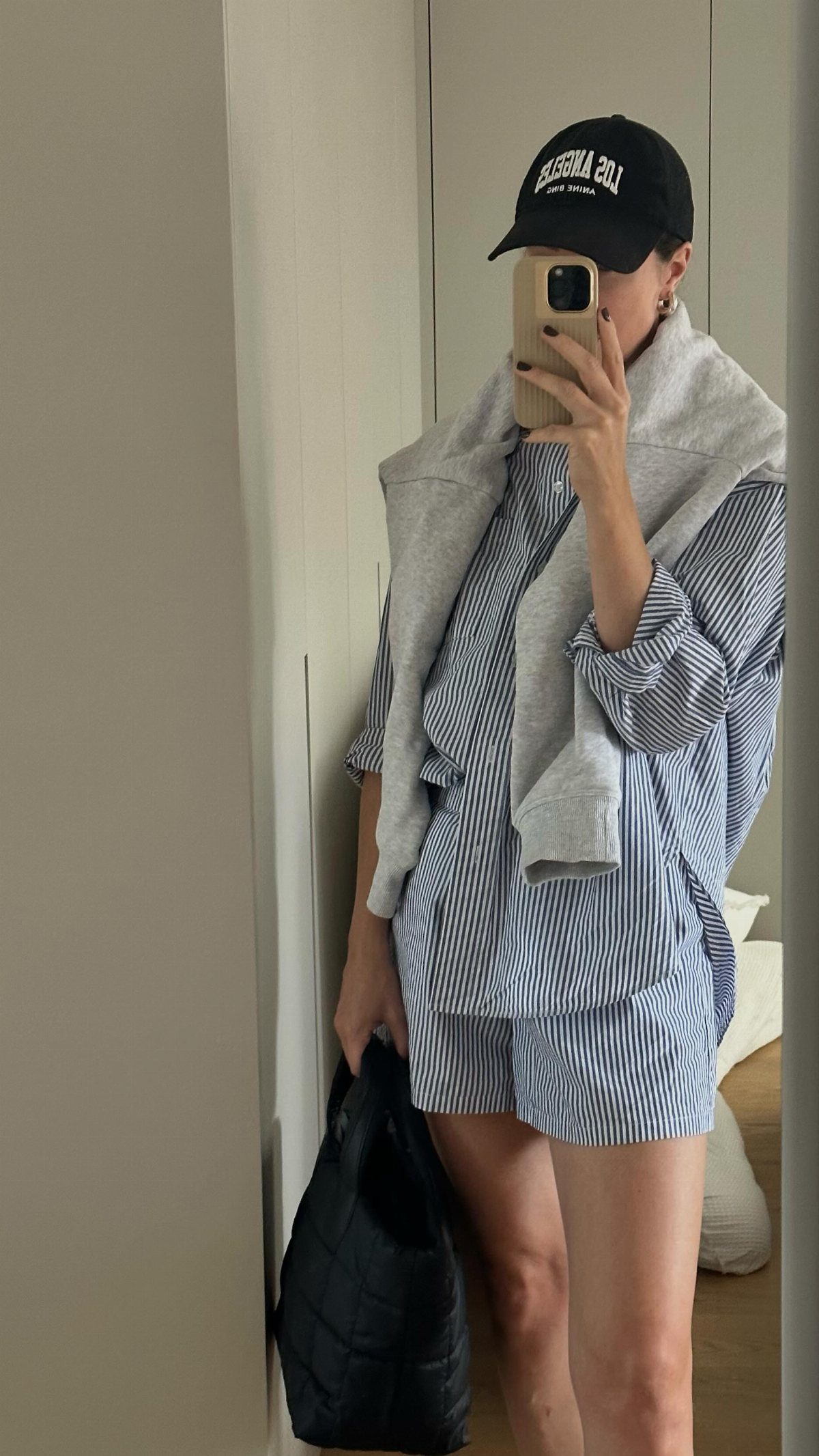 Person in blue striped shirt and shorts with a grey sweatshirt draped over shoulders.