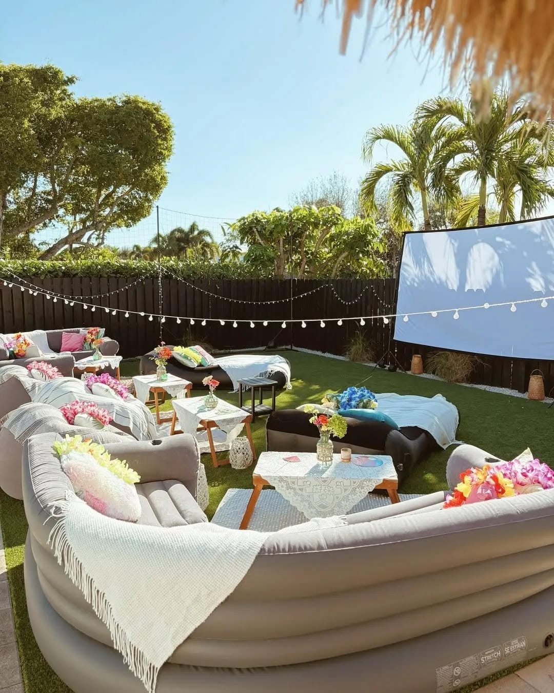 Inflatable sofas and small tables arranged on artificial turf in a backyard with a large projector screen.