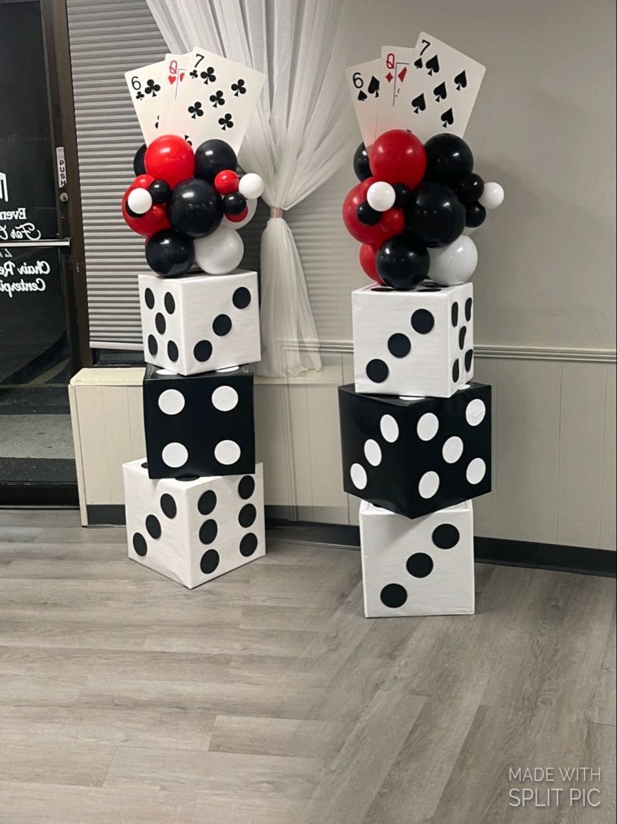 Two balloon pillars decorated with dice-patterned boxes and playing cards stand against a white curtain.