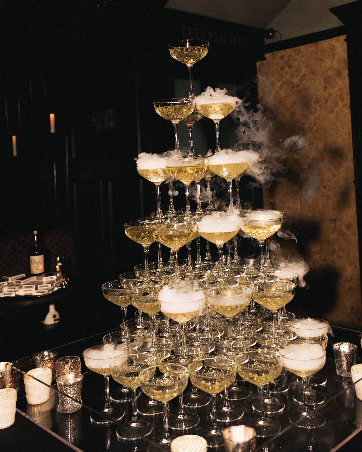 A tall champagne tower of sparkling glasses with white vapor rising in a dark room.