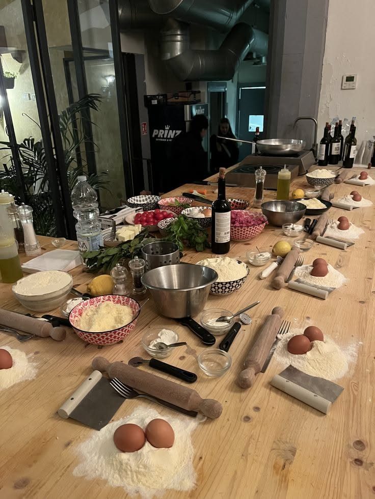 A wooden table prepared with flour, eggs, rolling pins, and various ingredients for a cooking class.
