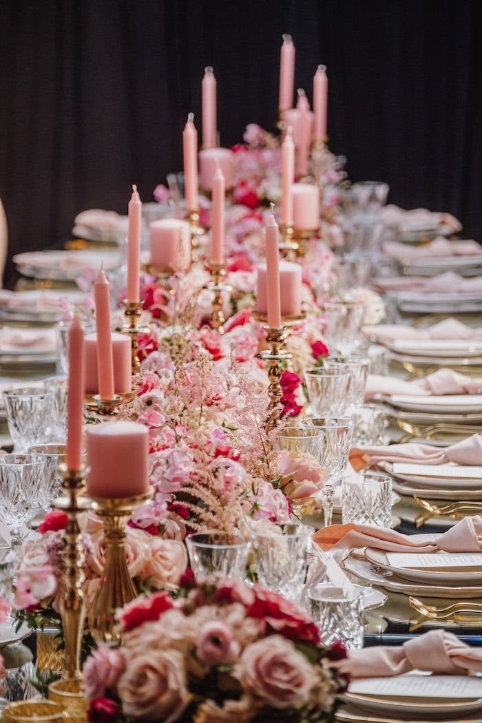 An elegant dinner table decorated with pink flowers, pink candles, and crystal glassware.