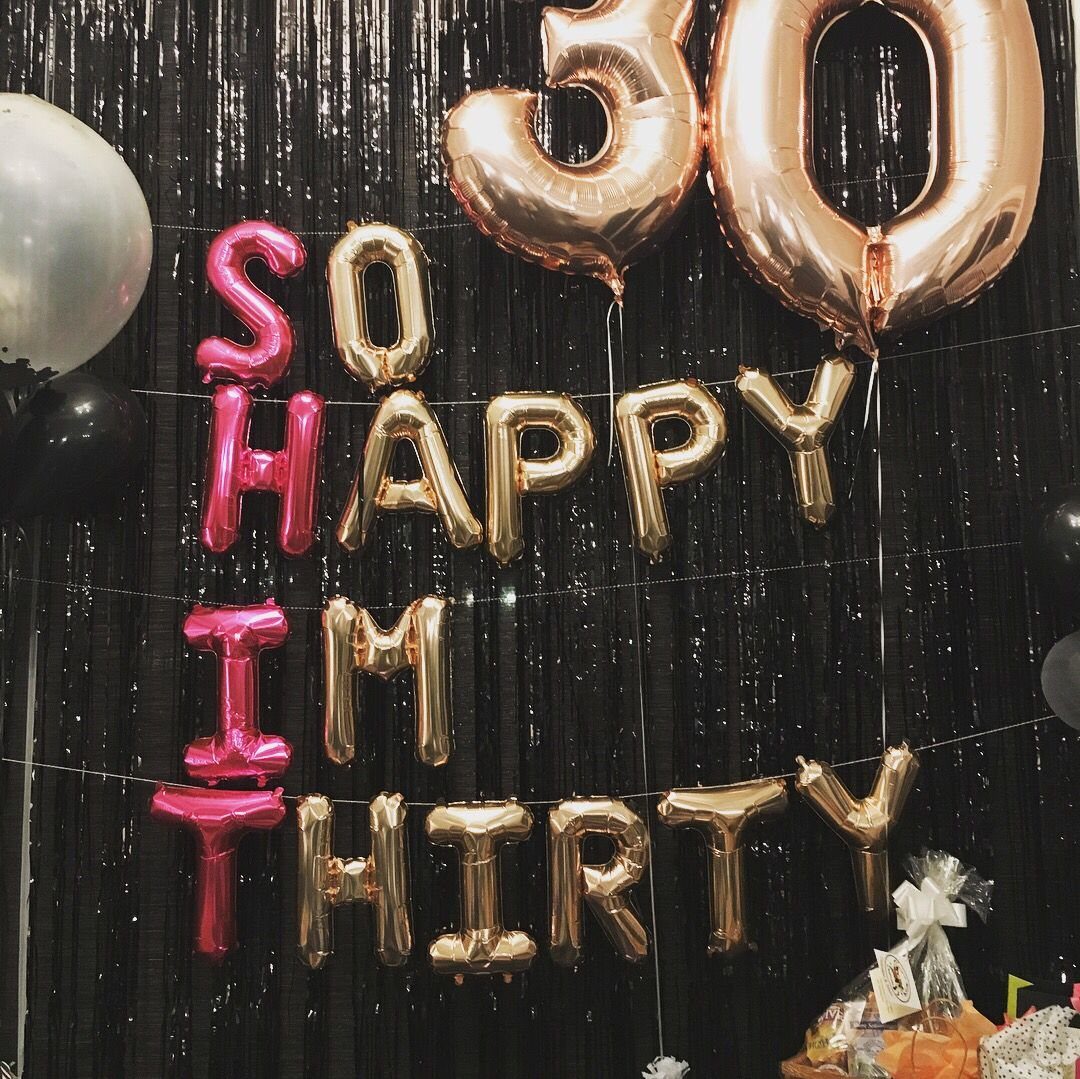 Gold and pink foil balloons spelling 'SO HAPPY IM THIRTY' against a black fringe backdrop.