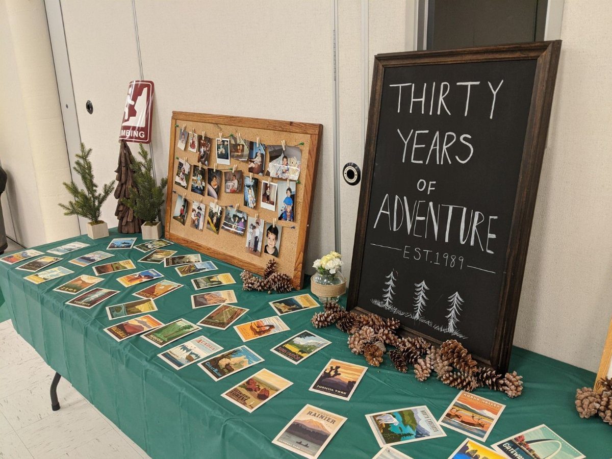 A green table decorated with a chalkboard sign, landscape postcards, and small pine trees.