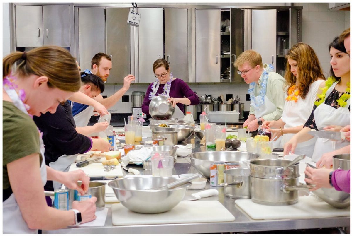 Group of people in aprons preparing food together in a professional kitchen setting.