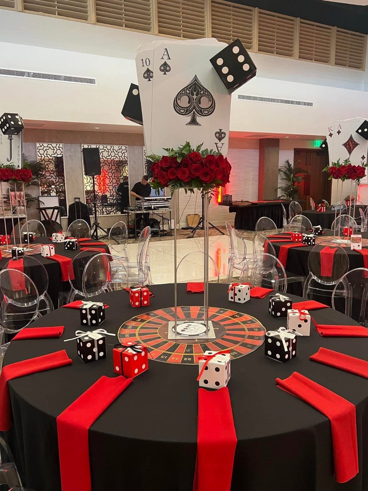 A banquet table decorated with playing cards, red roses, dice, and black and white gift boxes.